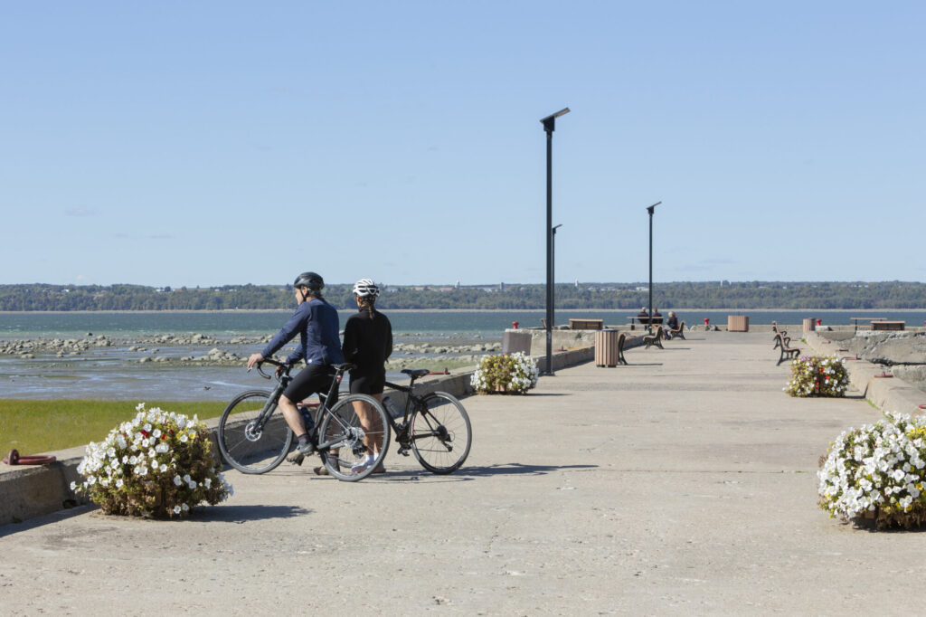 Deux cyclistes sur un quai fleuri au bord du fleuve Saint-Laurent dans Lotbinière