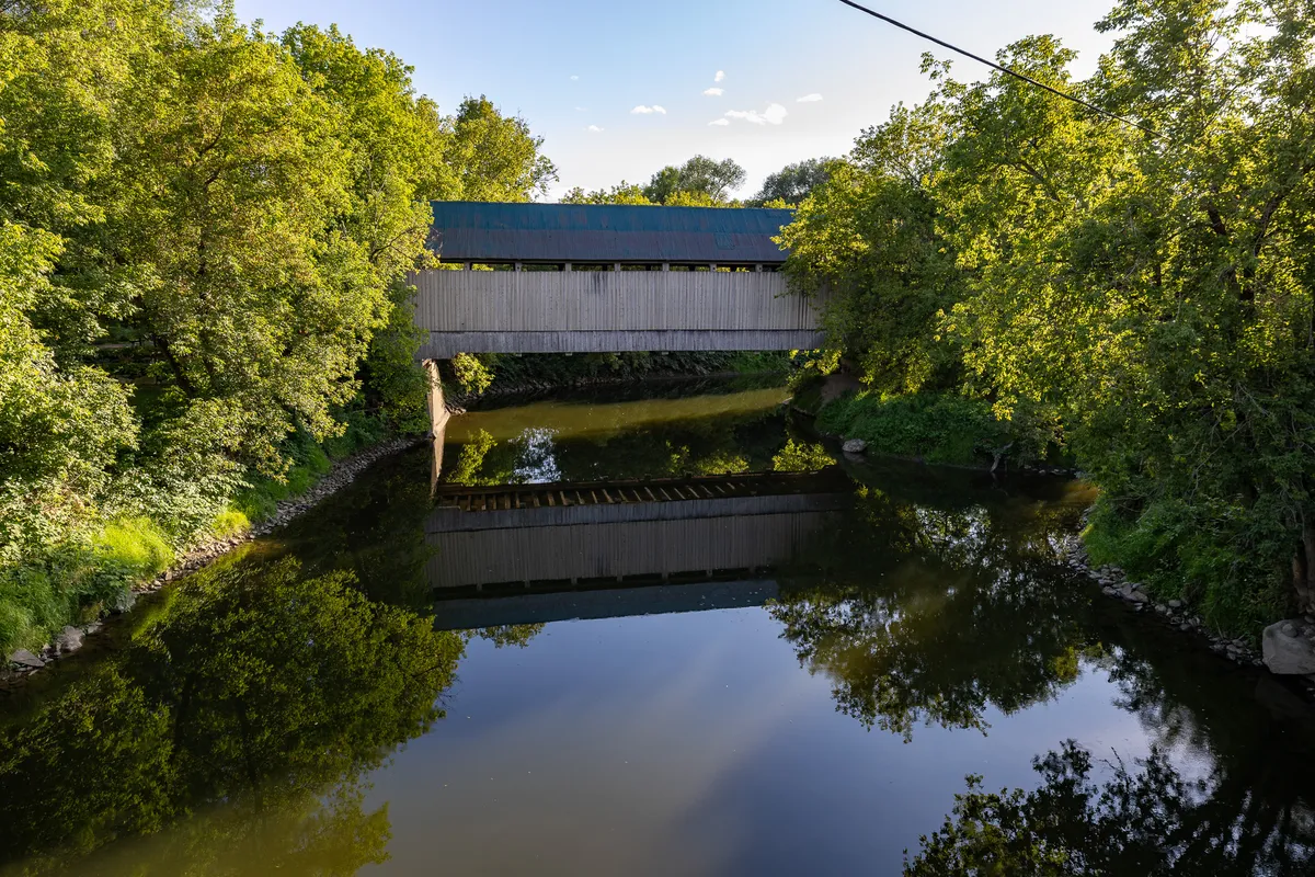 Road trip Chemin des Cantons : pont couvert en bois au-dessus d'une rivière calme, secteur de Compton, en été