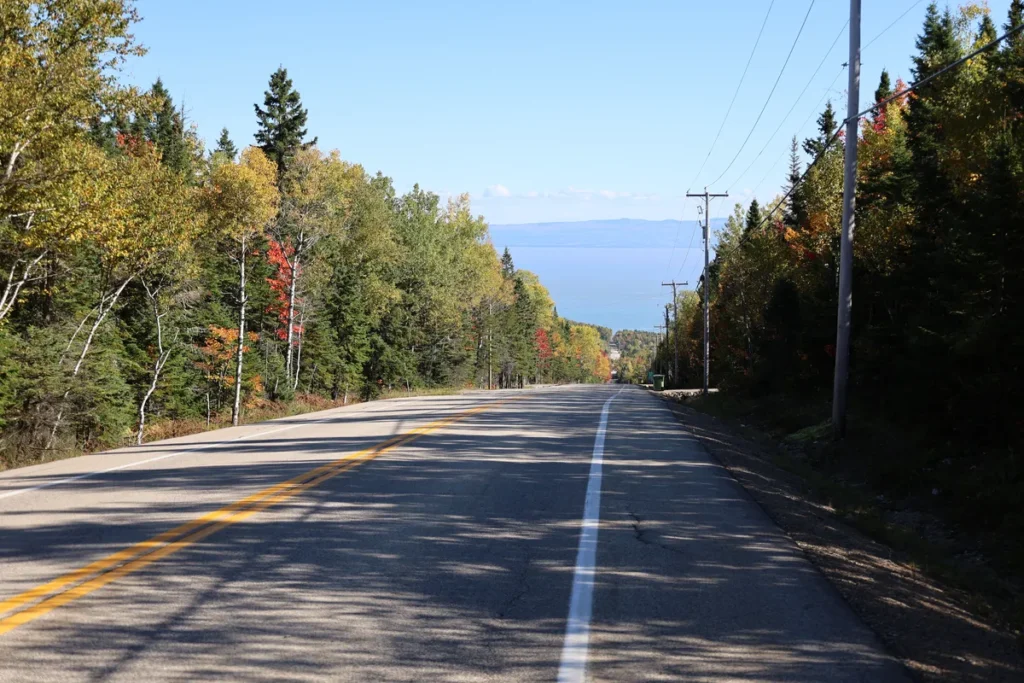 Couleurs d’automne dans Charlevoix : route bordée d’érables rouges et de bouleaux jaunis qui descend vers le fleuve
