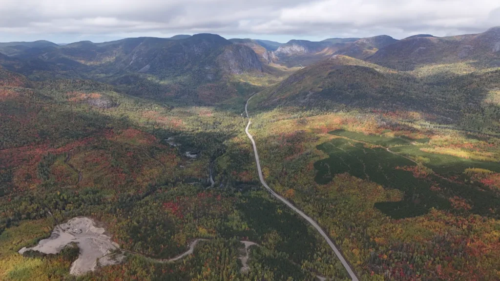 Couleurs d’automne dans Charlevoix : vallée rouge et orange traversée par une route, vue du ciel, au nord de Saint-Urbain