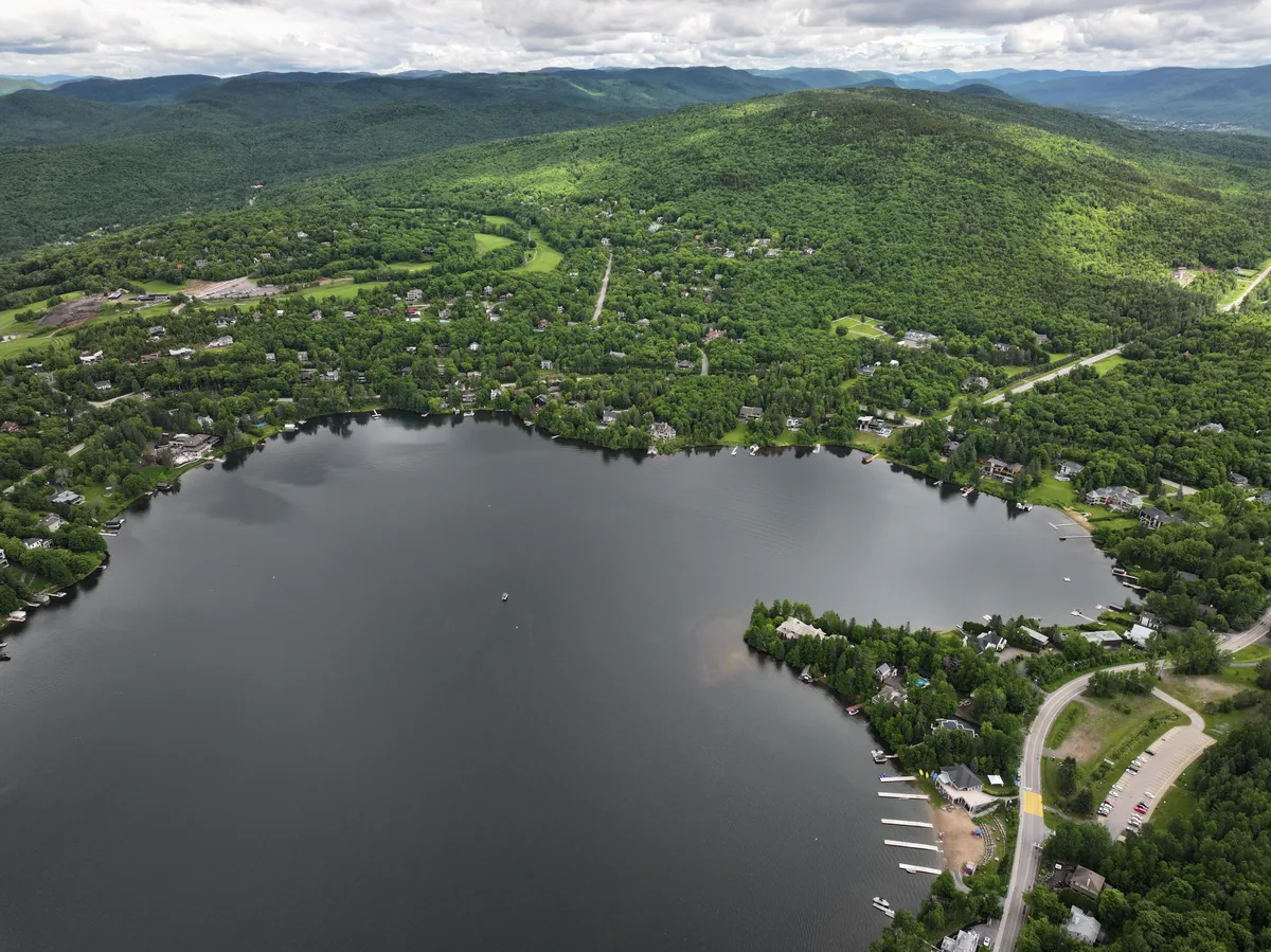 Vue aérienne du lac Beauport en été, avec sa plage, ses quais et le village entouré de montagnes boisées