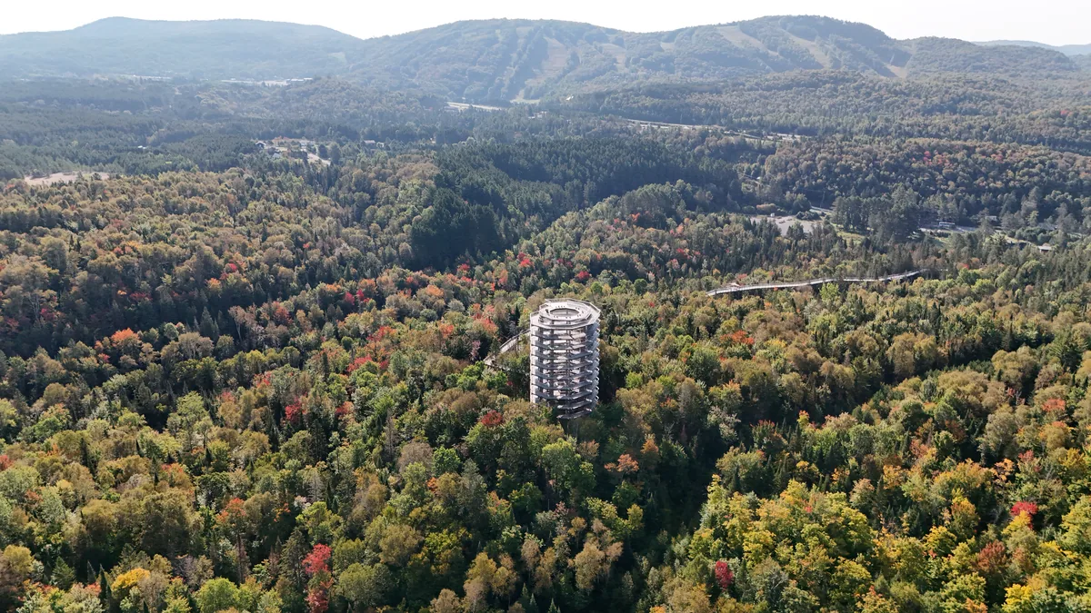 Vue aérienne de la tour du Sentier des Cimes dans une forêt qui rougit, avec les pistes du mont Tremblant en arrière-plan