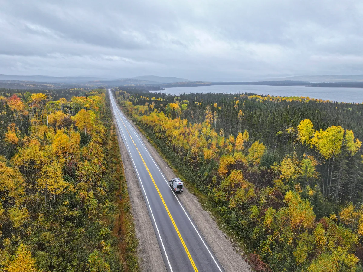 Route 167 bordée de forêt boréale en octobre, avec un lac à l'horizon