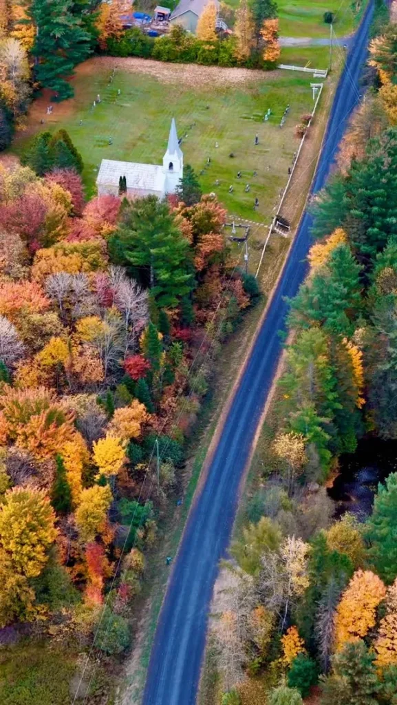 Route de campagne bordée d'arbres d'automne et église blanche dans les Cantons-de-l'Est, vue des airs