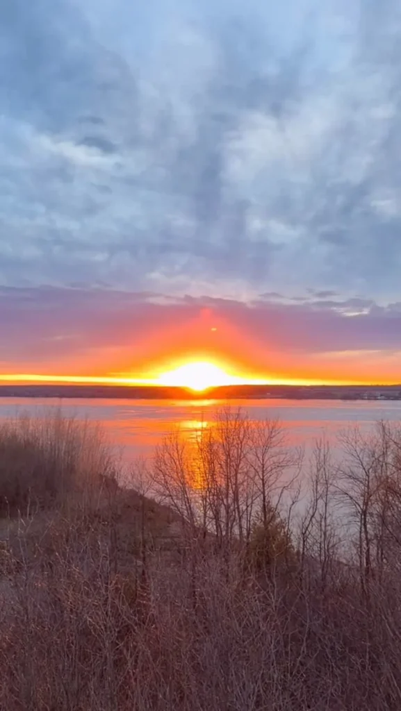Coucher de soleil sur une large rivière bordée d'arbustes au début du printemps
